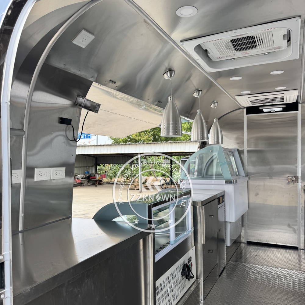 Interior rendering of a food trailer kitchen with stainless steel counters, refrigerator, ice cream showcase, and pendant lights